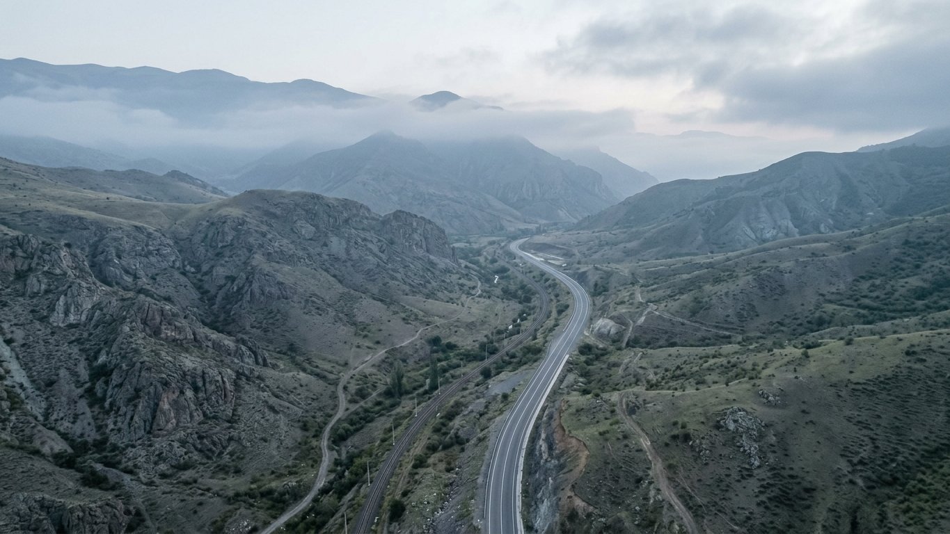 Aerial view of the mountain landscape of Syunik province in southern Armenia at dawn, with a single road or rail line cutting through the valley.